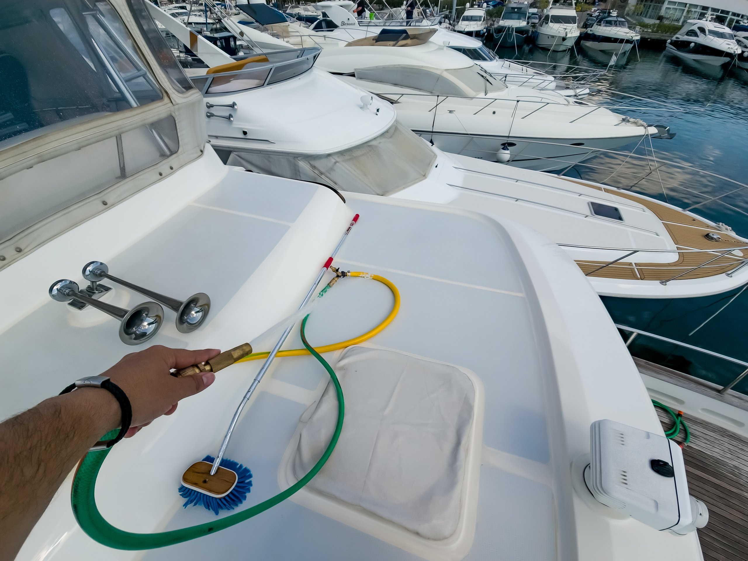 Close-up perspective of marine maintenance professional using specialized cleaning brush on white yacht deck