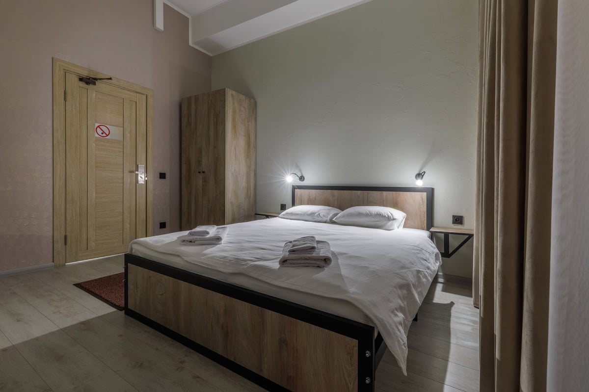 Modern minimalist hotel room featuring a wooden double bed with white linens