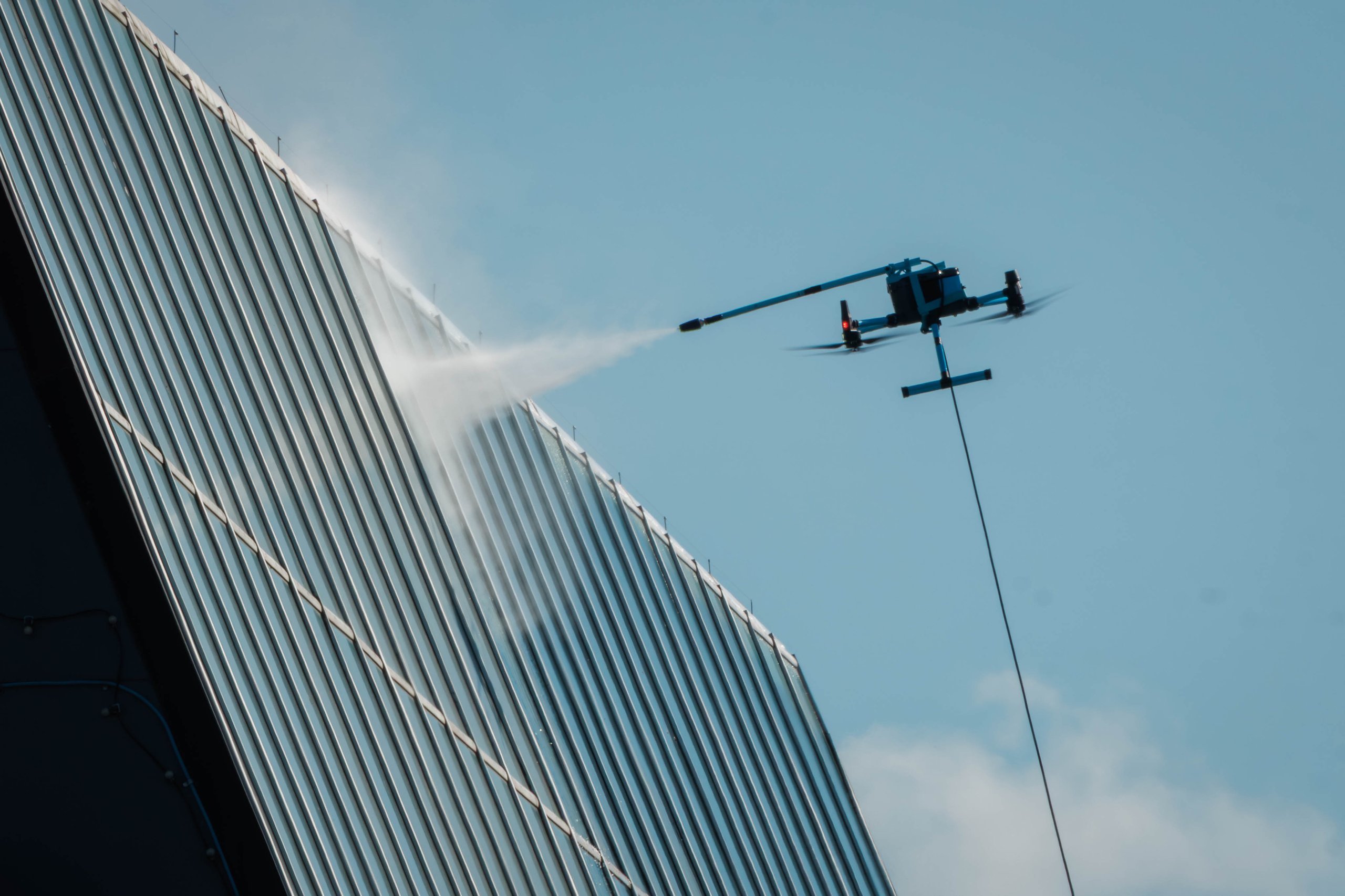 Autonomous drone hovers beside a glass-clad high-rise, spraying water for facade cleaning